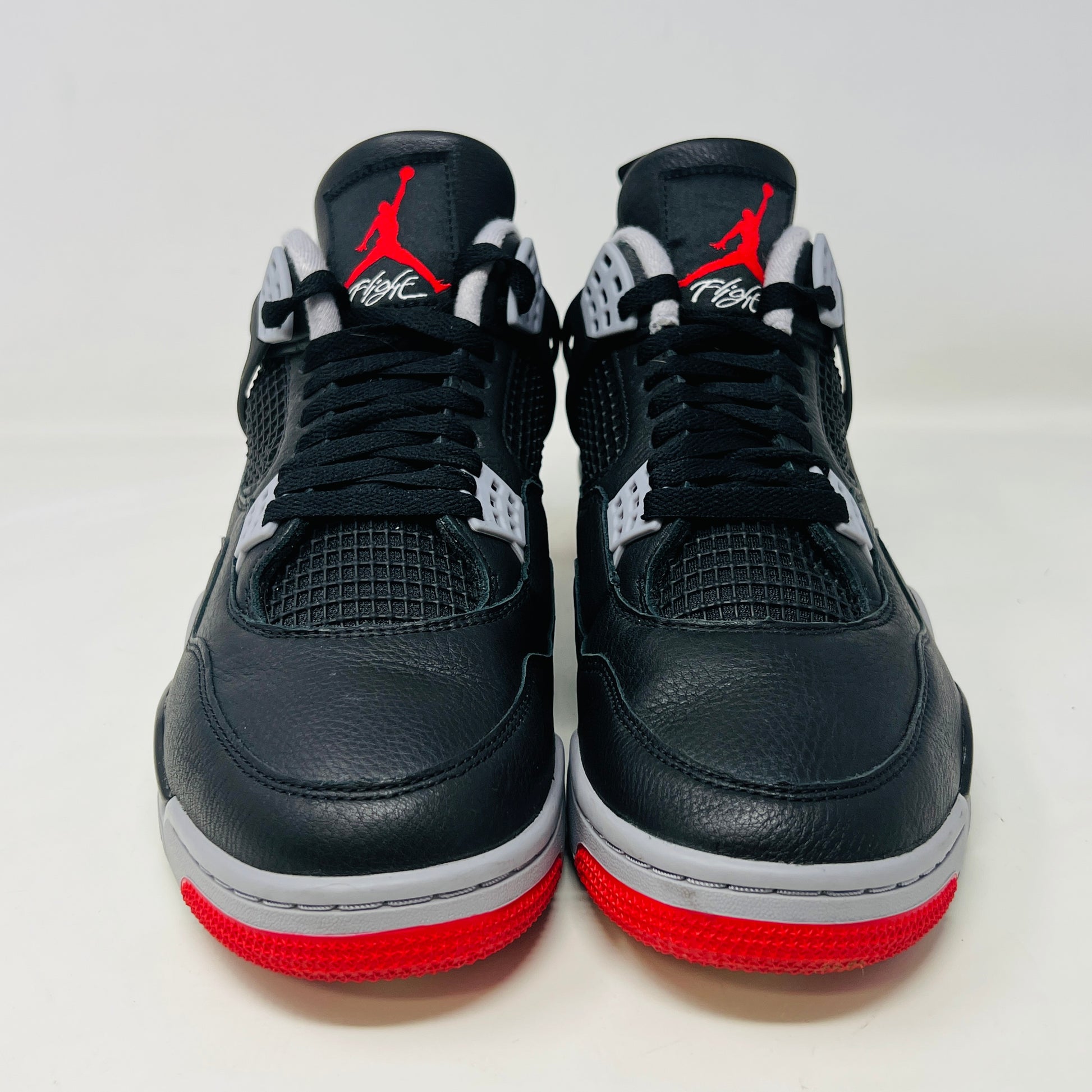 A Jordan 4 Retro Bred Reimagined sneaker in black and red sits on its good condition box, showcasing textured black leather uppers, red accents, and a white midsole. The box has a speckled design featuring the iconic Nike Air logo.