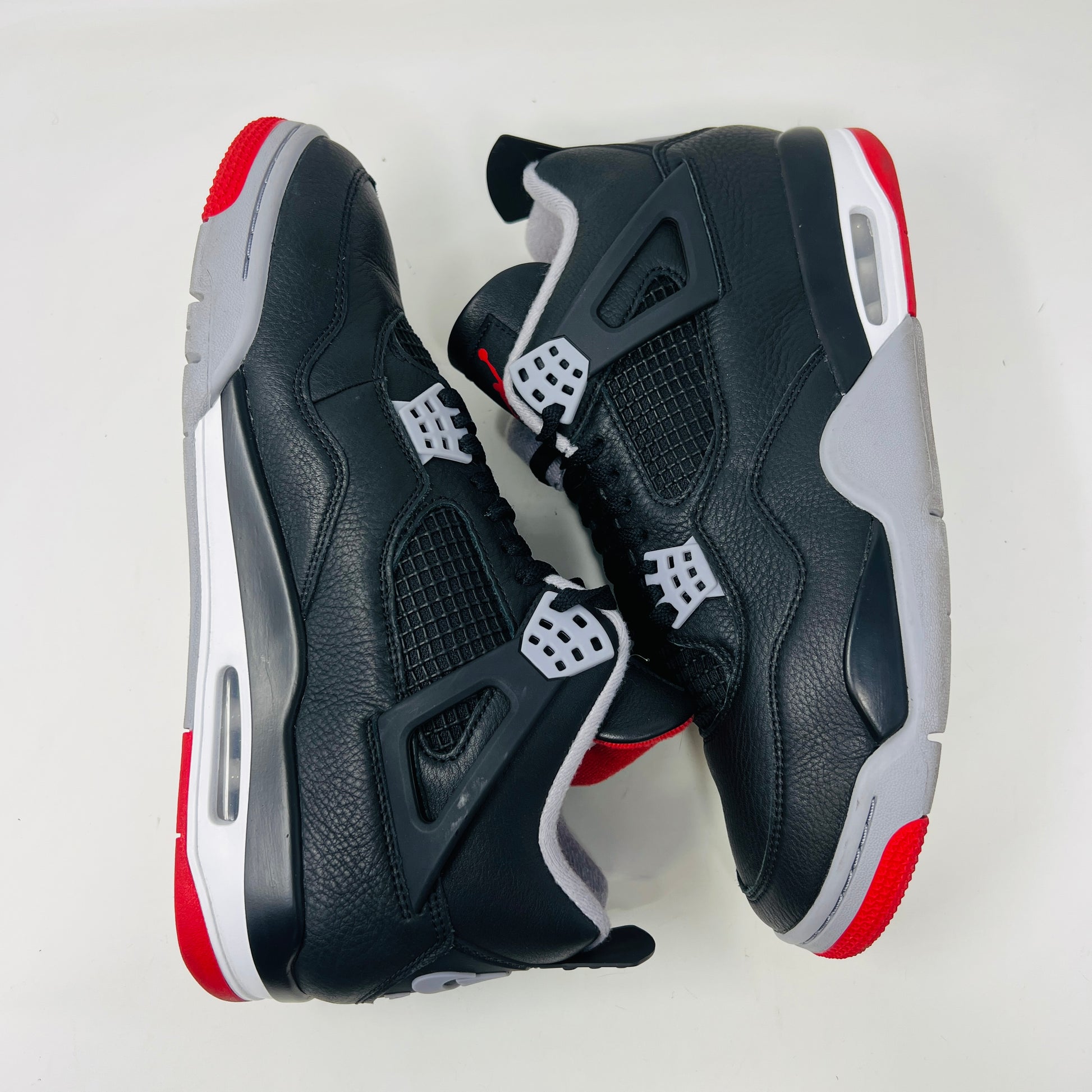 A Jordan 4 Retro Bred Reimagined sneaker in black and red sits on its good condition box, showcasing textured black leather uppers, red accents, and a white midsole. The box has a speckled design featuring the iconic Nike Air logo.