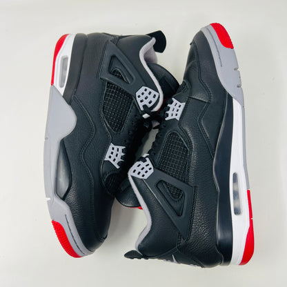 A Jordan 4 Retro Bred Reimagined sneaker in black and red sits on its good condition box, showcasing textured black leather uppers, red accents, and a white midsole. The box has a speckled design featuring the iconic Nike Air logo.