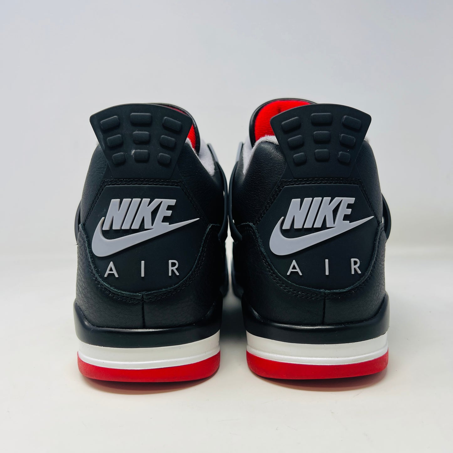 A Jordan 4 Retro Bred Reimagined sneaker in black and red sits on its good condition box, showcasing textured black leather uppers, red accents, and a white midsole. The box has a speckled design featuring the iconic Nike Air logo.