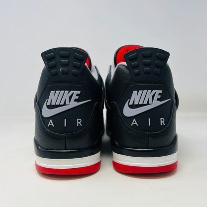 A Jordan 4 Retro Bred Reimagined sneaker in black and red sits on its good condition box, showcasing textured black leather uppers, red accents, and a white midsole. The box has a speckled design featuring the iconic Nike Air logo.