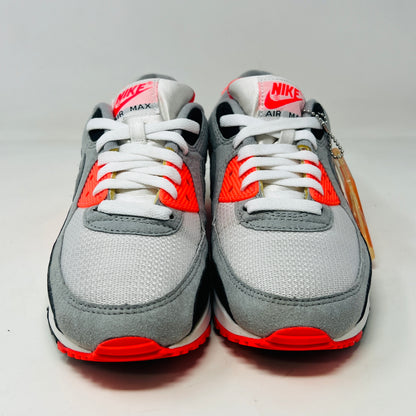 The Nike Air Max 90 Infrared (2020) sneaker in grey, black, and red sits on a red Nike box. Nearby are Anatomically Arched Orthotics insoles in a clear package. The shoe showcases clean uppers and an attached hang tag for a sleek look.