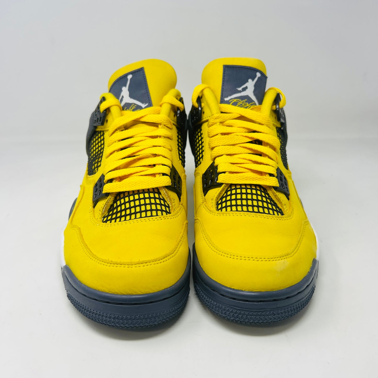 The Jordan 4 Retro Lightning (2021) sneakers have yellow uppers with black and white accents, visible air cushioning, and distinctive side netting. They come in a matching yellow and gray speckled box, ideal for everyday style.