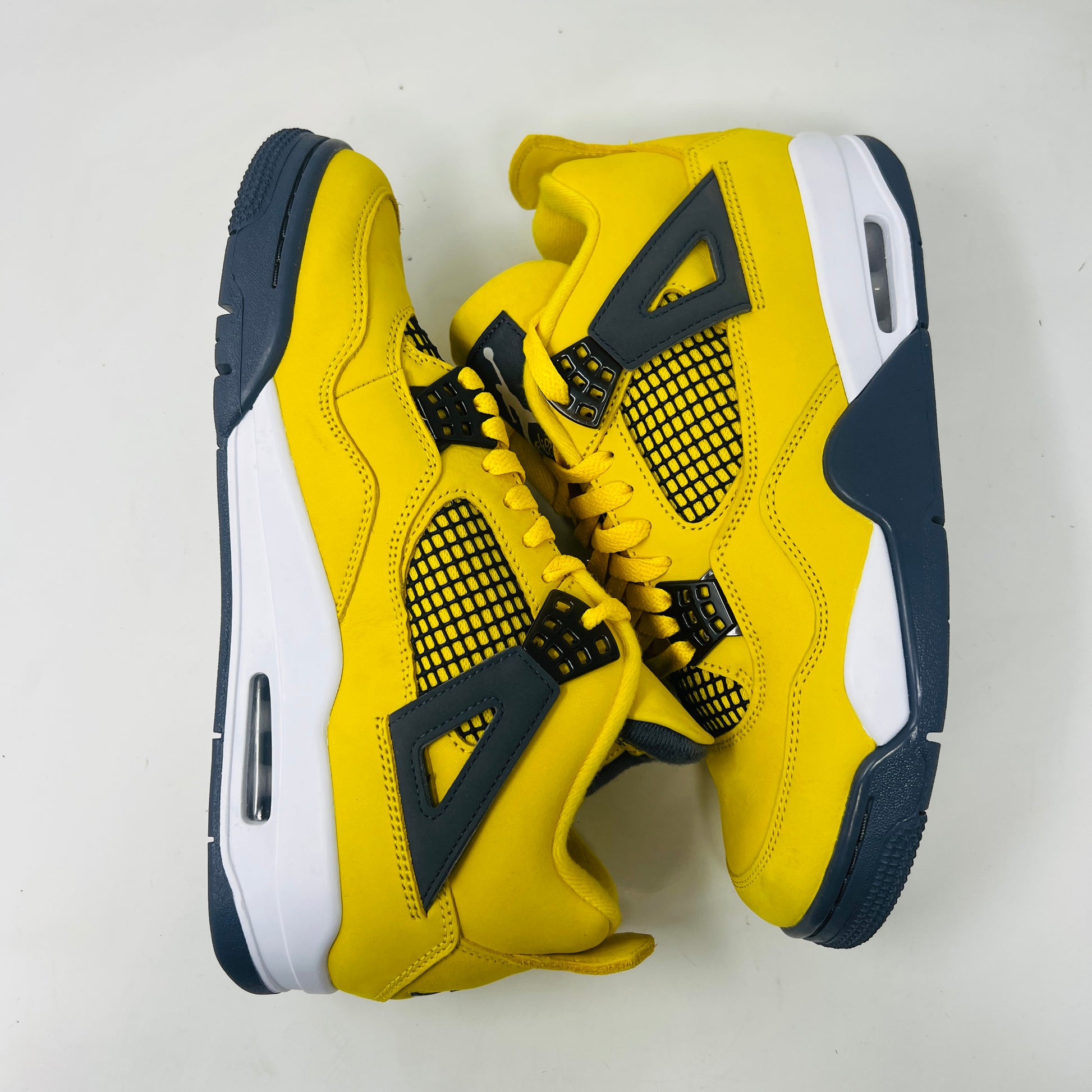 The Jordan 4 Retro Lightning (2021) sneakers have yellow uppers with black and white accents, visible air cushioning, and distinctive side netting. They come in a matching yellow and gray speckled box, ideal for everyday style.