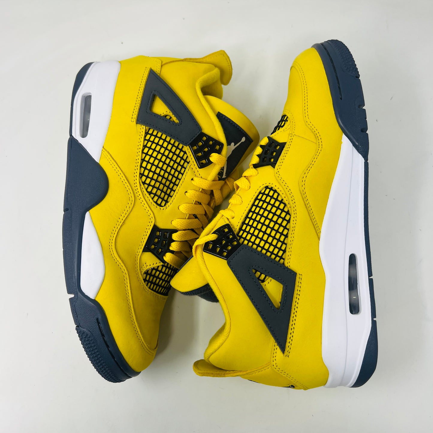 The Jordan 4 Retro Lightning (2021) sneakers have yellow uppers with black and white accents, visible air cushioning, and distinctive side netting. They come in a matching yellow and gray speckled box, ideal for everyday style.