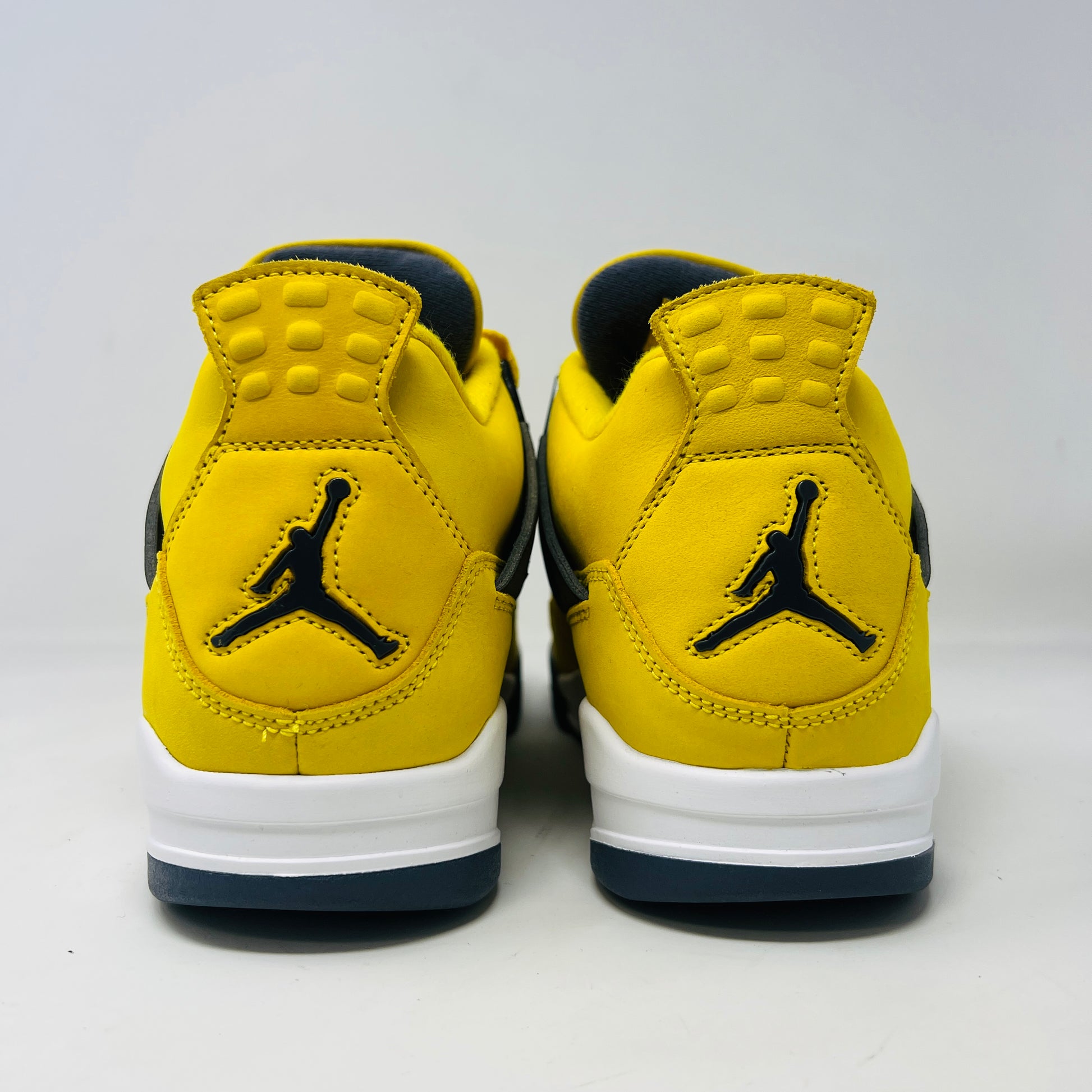 The Jordan 4 Retro Lightning (2021) sneakers have yellow uppers with black and white accents, visible air cushioning, and distinctive side netting. They come in a matching yellow and gray speckled box, ideal for everyday style.