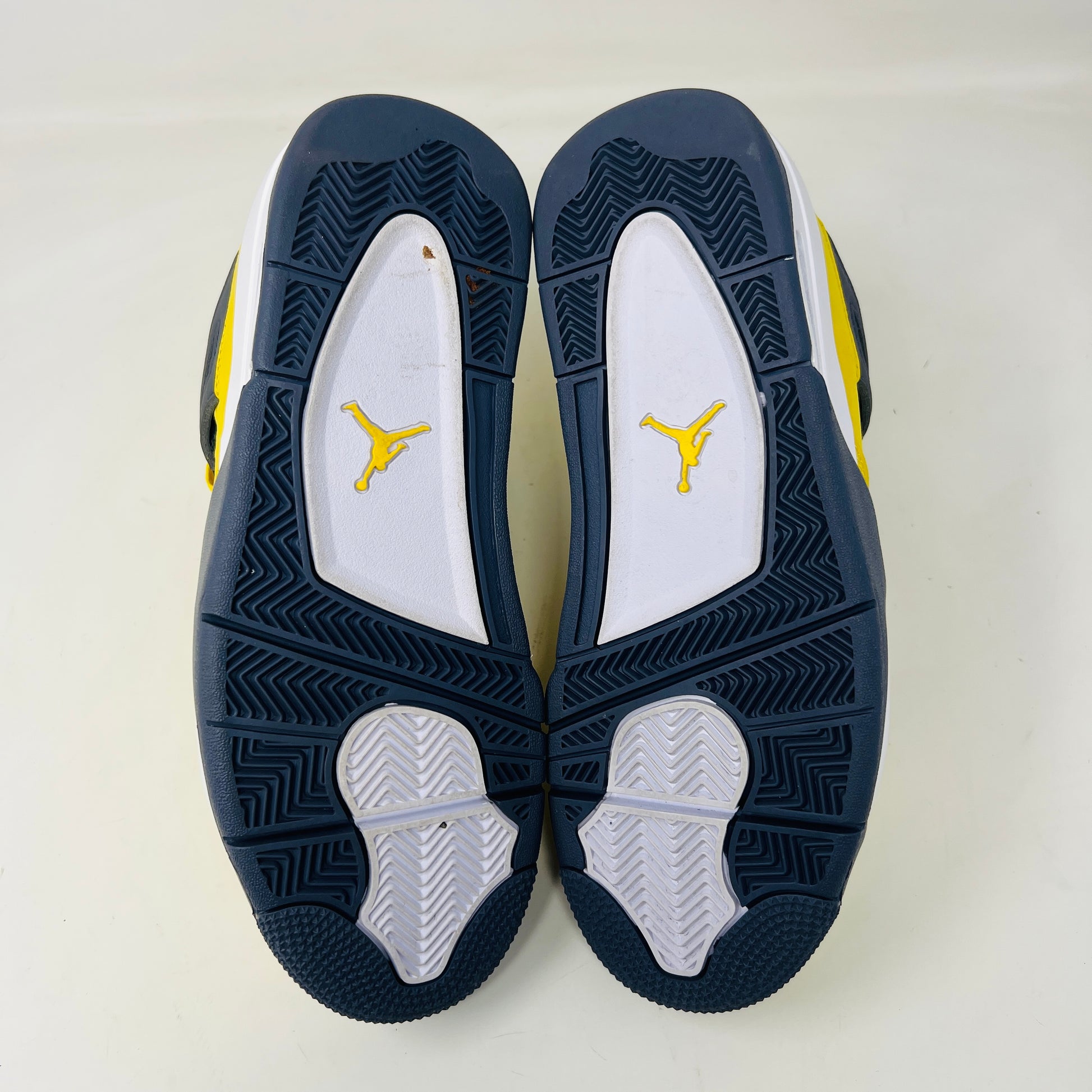 The Jordan 4 Retro Lightning (2021) sneakers have yellow uppers with black and white accents, visible air cushioning, and distinctive side netting. They come in a matching yellow and gray speckled box, ideal for everyday style.