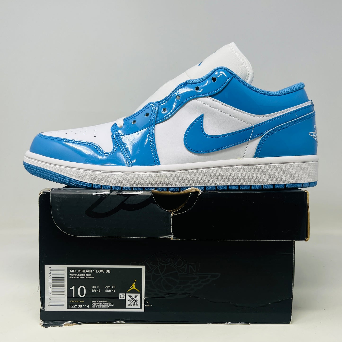 A pair of Jordan 1 Low SE White Legend Blue sneakers is elegantly displayed on a DMG box, featuring the iconic Nike swoosh and Wings logo on the heel. The sleek black box showcases the 2024 size label and brand logo.