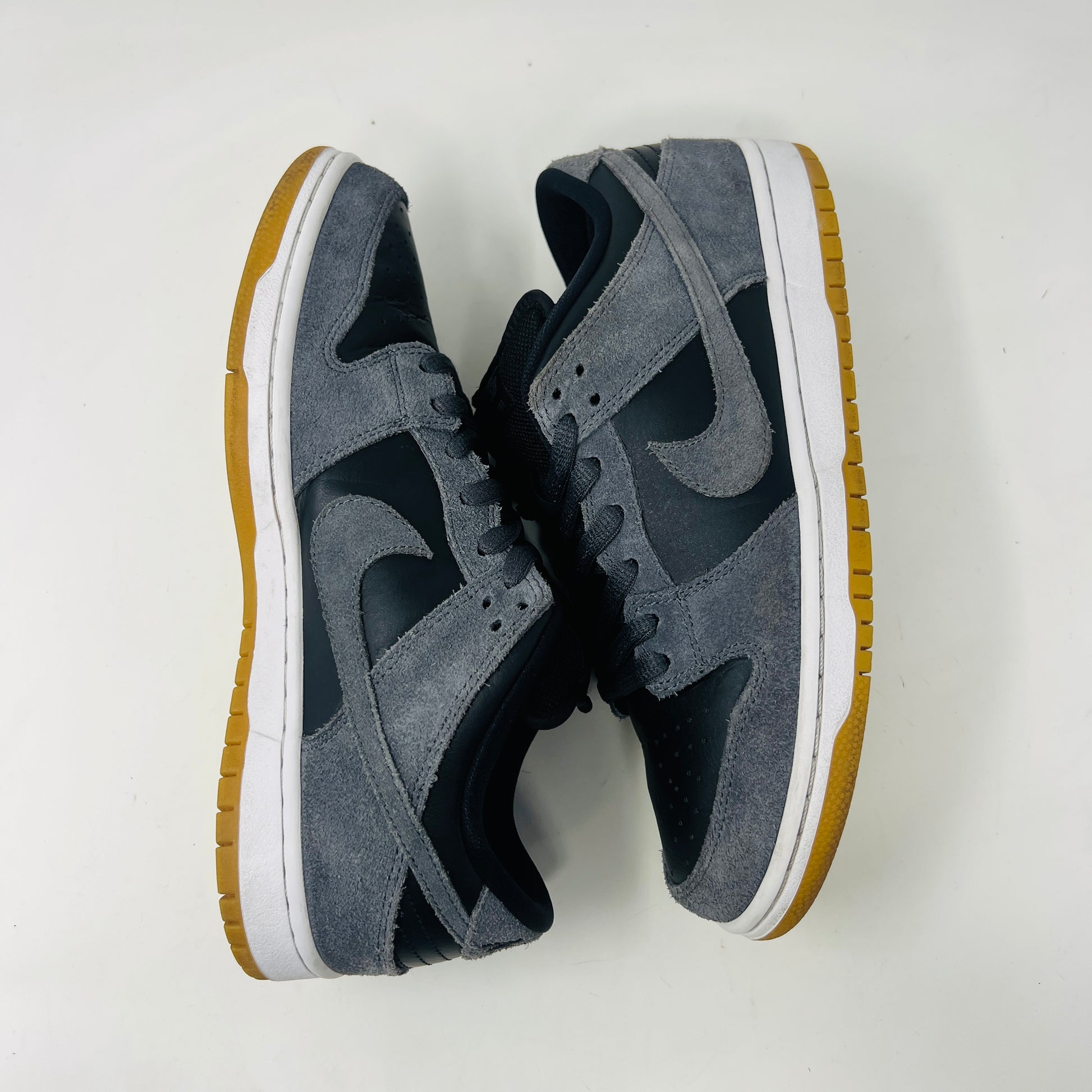 Displayed on a turquoise box, the 2018 Nike SB Dunk Low Dark Grey Black Gum shoe features gray suede uppers, a black Swoosh, and a gum sole. The slightly opened lid reveals product details inside.