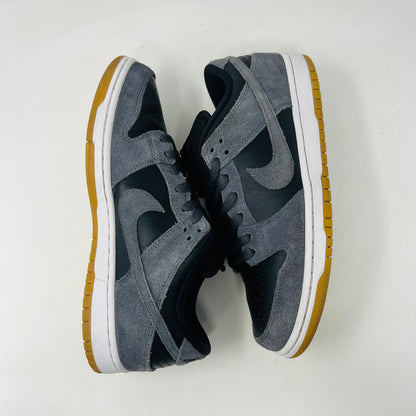 Displayed on a turquoise box, the 2018 Nike SB Dunk Low Dark Grey Black Gum shoe features gray suede uppers, a black Swoosh, and a gum sole. The slightly opened lid reveals product details inside.