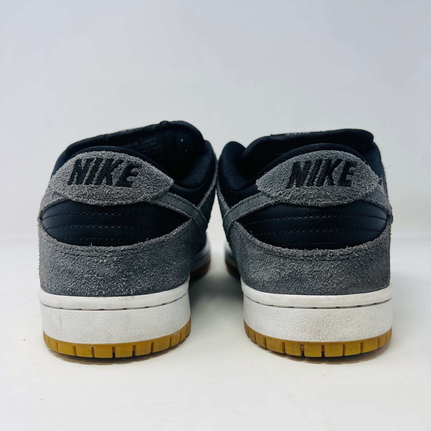 Displayed on a turquoise box, the 2018 Nike SB Dunk Low Dark Grey Black Gum shoe features gray suede uppers, a black Swoosh, and a gum sole. The slightly opened lid reveals product details inside.