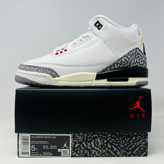 The Jordan 3 Retro White Cement Reimagined (GS) sneaker by Jordan, in white with gray and black elephant print accents, is displayed on a pristine black box. The box features the Jumpman logo with size and style details, ensuring the shoes include all necessary accessories.