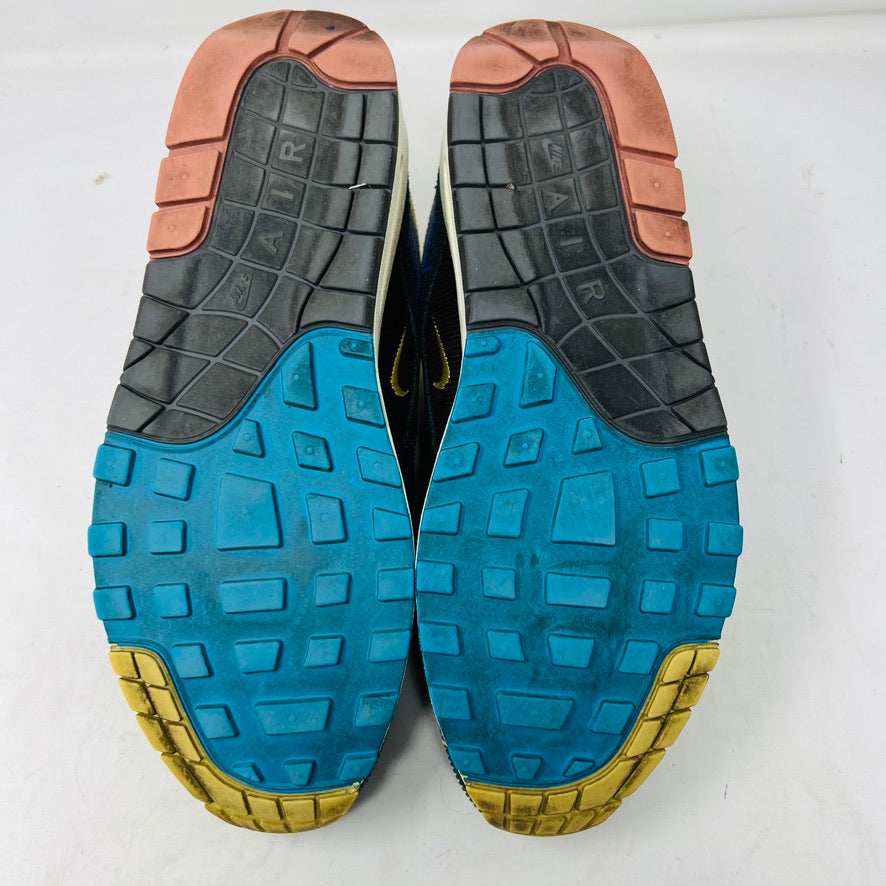 The Nike Air Max 1/97 Sean Wotherspoon sneakers feature a layered design in yellow, blue, pink, and gray with a wave logo on the tongue. These authentic shoes have a textured upper stitched intricately for an eye-catching finish against a white background.