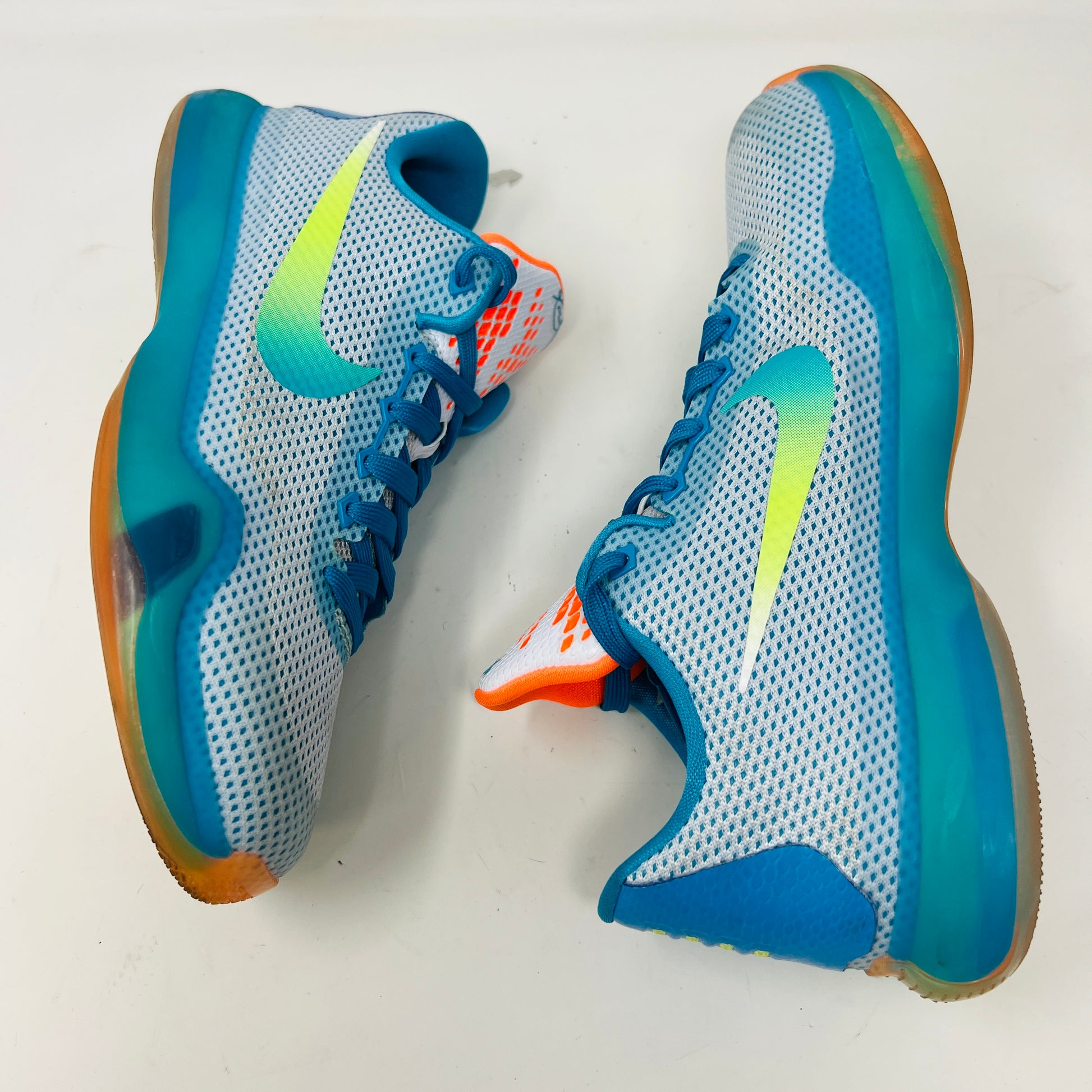 The Kobe 10 GS High Dive from Nike, in size 7Y, is on display with a blue upper, gradient yellow-green Swoosh, orange lining, and a multicolored sole. Its resting on its black box and shows normal wear.