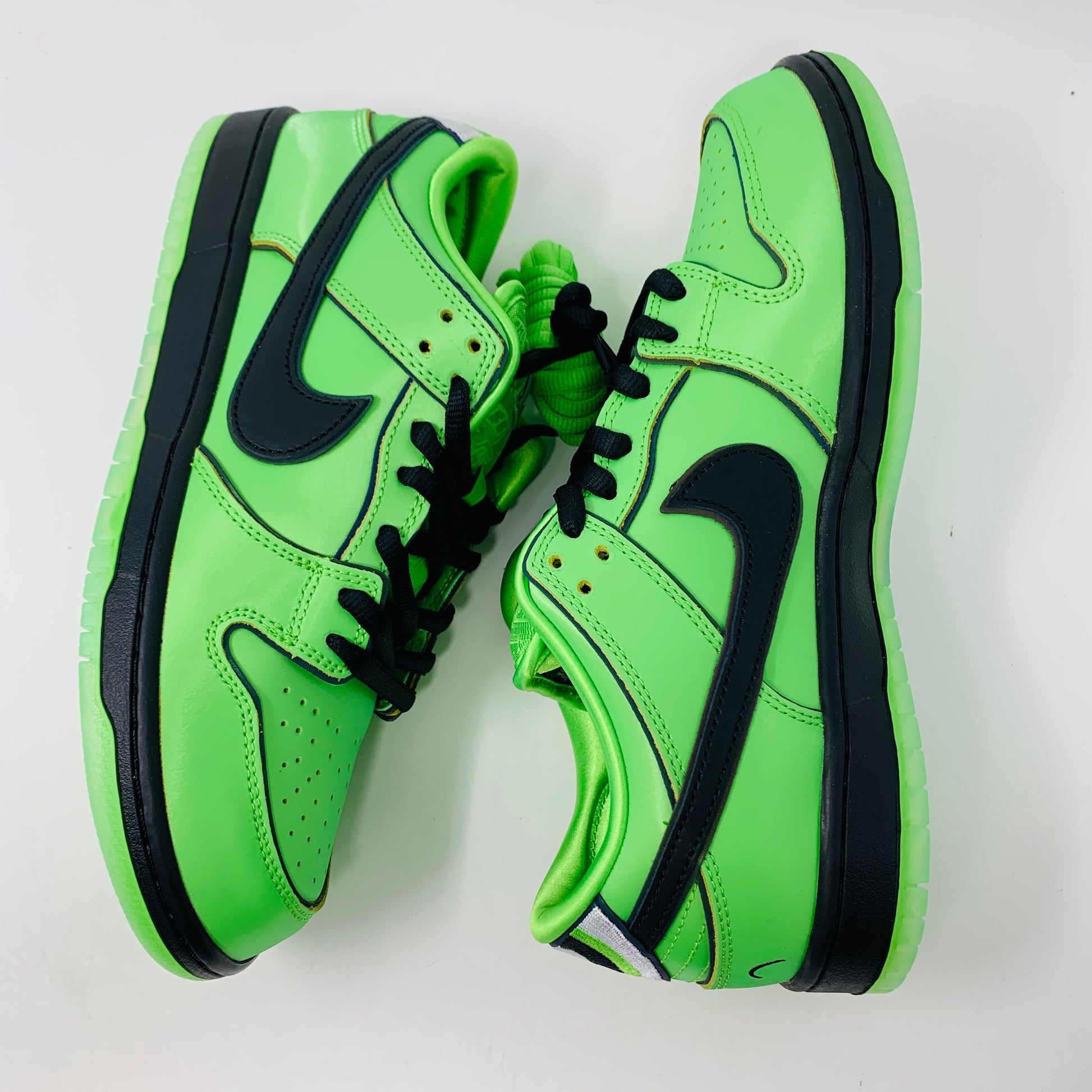 The Nike SB Dunk Low The Powerpuff Girls Buttercup sneakers, featuring a vibrant green color with black laces and a black swoosh logo, are displayed side by side on a white background.