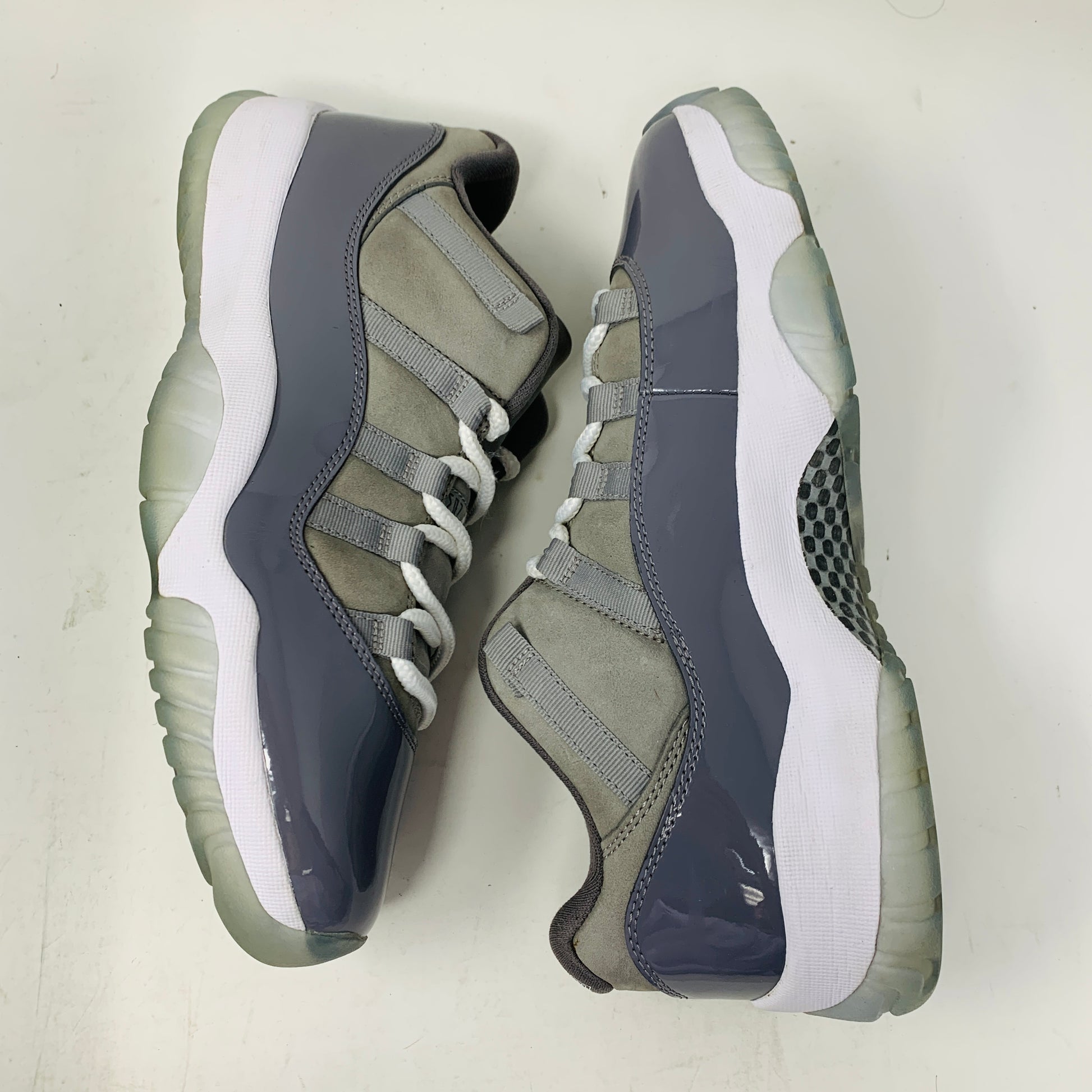 The Jordan 11 Retro Low Cool Grey by Jordan, in size 9.5, showcases sleek patent leather and mesh in gray and white with elegant white laces. Placed on a white surface, these stylish sneakers feature clean uppers and translucent soles for a contemporary look.