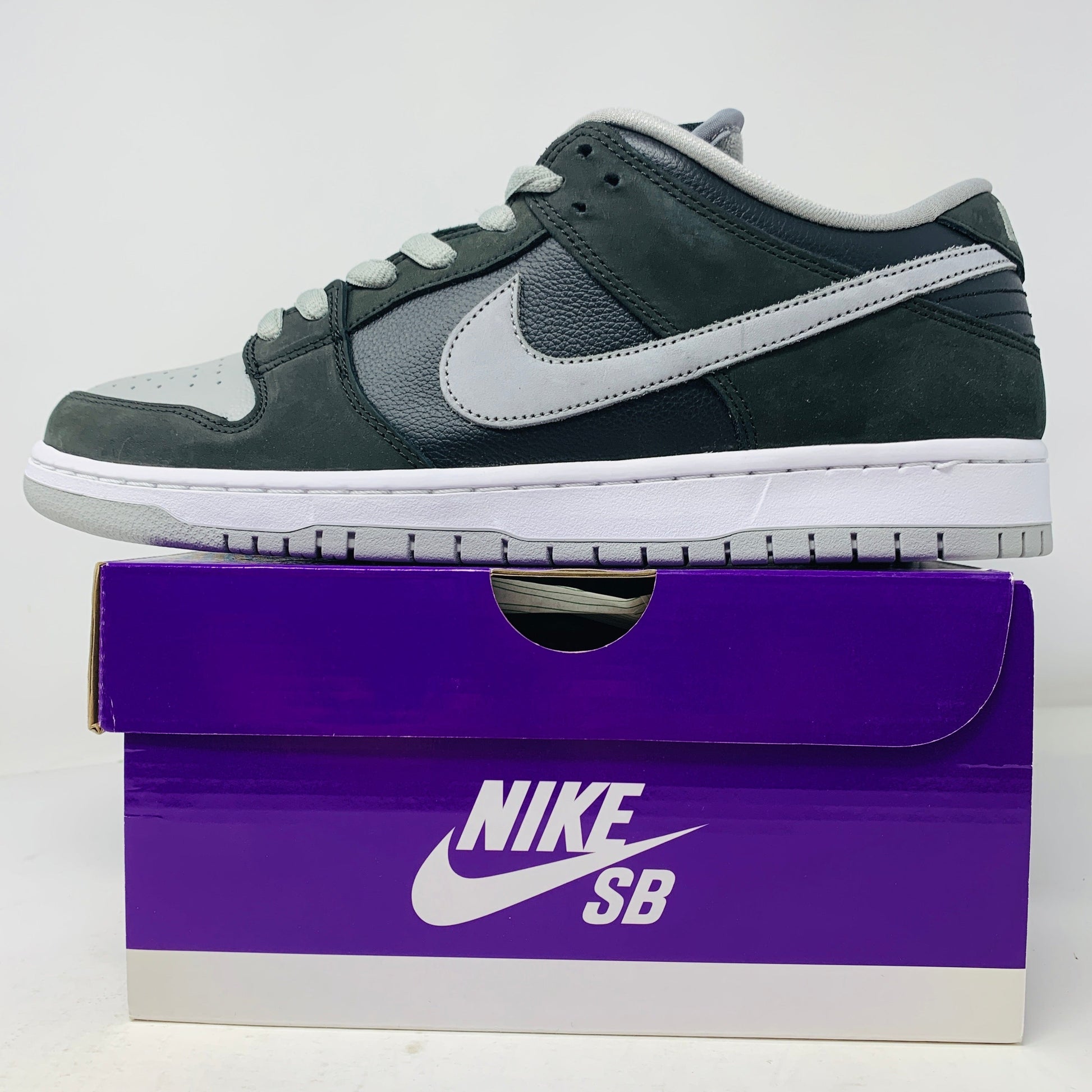 Nike SB Dunk Low J-Pack Shadow sneakers with grey laces on a purple box, brand new condition.