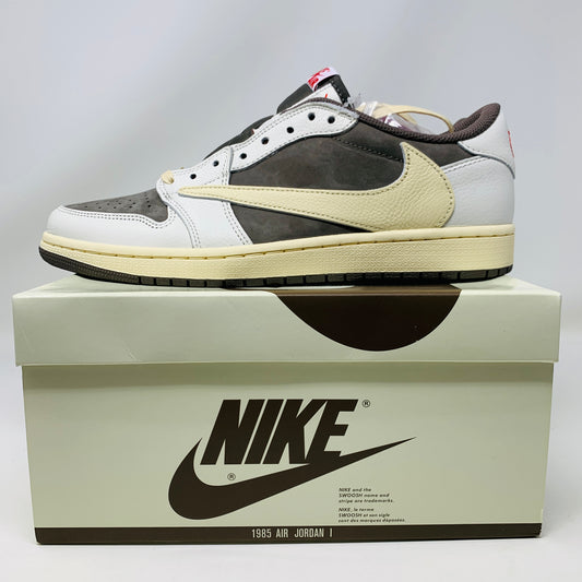 A brand new, 100% authentic pair of Jordan 1 Low Travis Scott Reverse Mocha sneakers in white, gray, and brown sit atop their matching box. The shoes feature a large swoosh on the side, while the box displays the Jordan logo and reads 1985 Air Jordan.