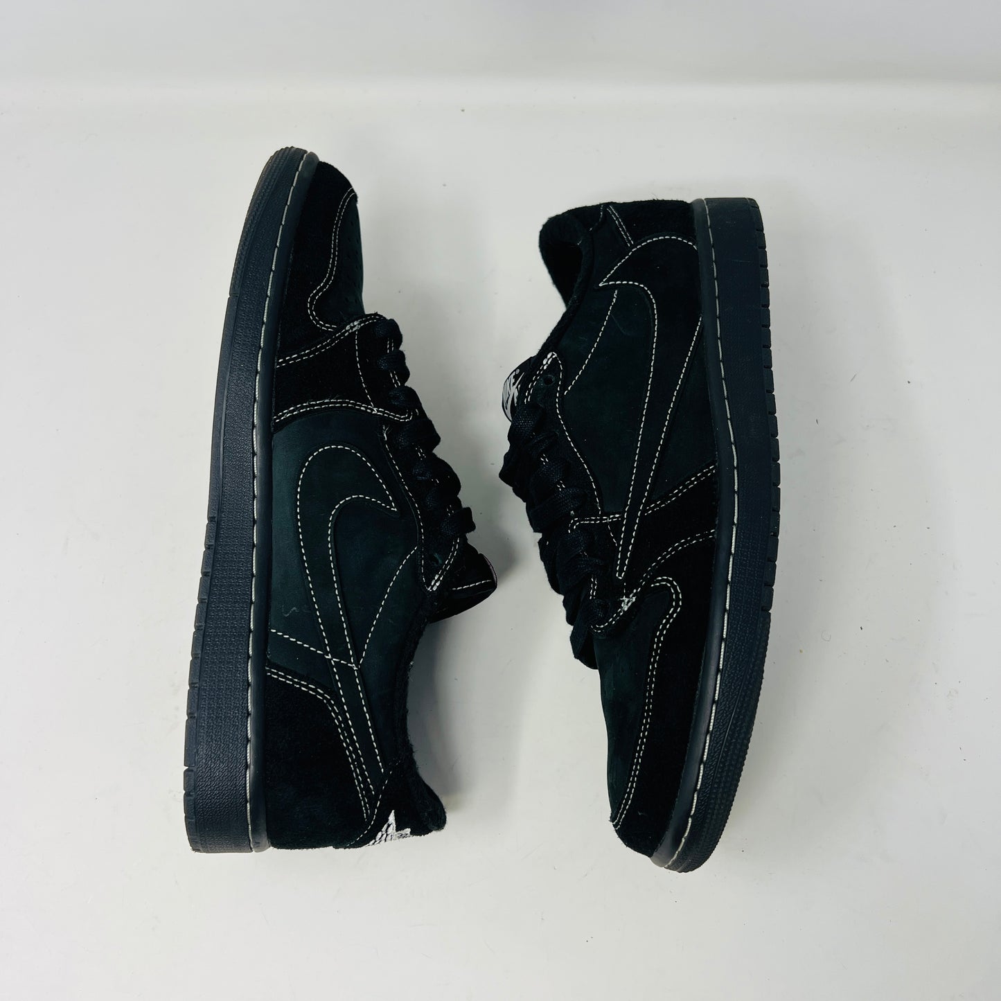 The Jordan 1 Retro Low OG SP Travis Scott Black Phantom sneaker, featuring clean black uppers with white stitching, is displayed on a black shoe box. It includes two sets of laces—one red and the other in a black-and-white pattern.