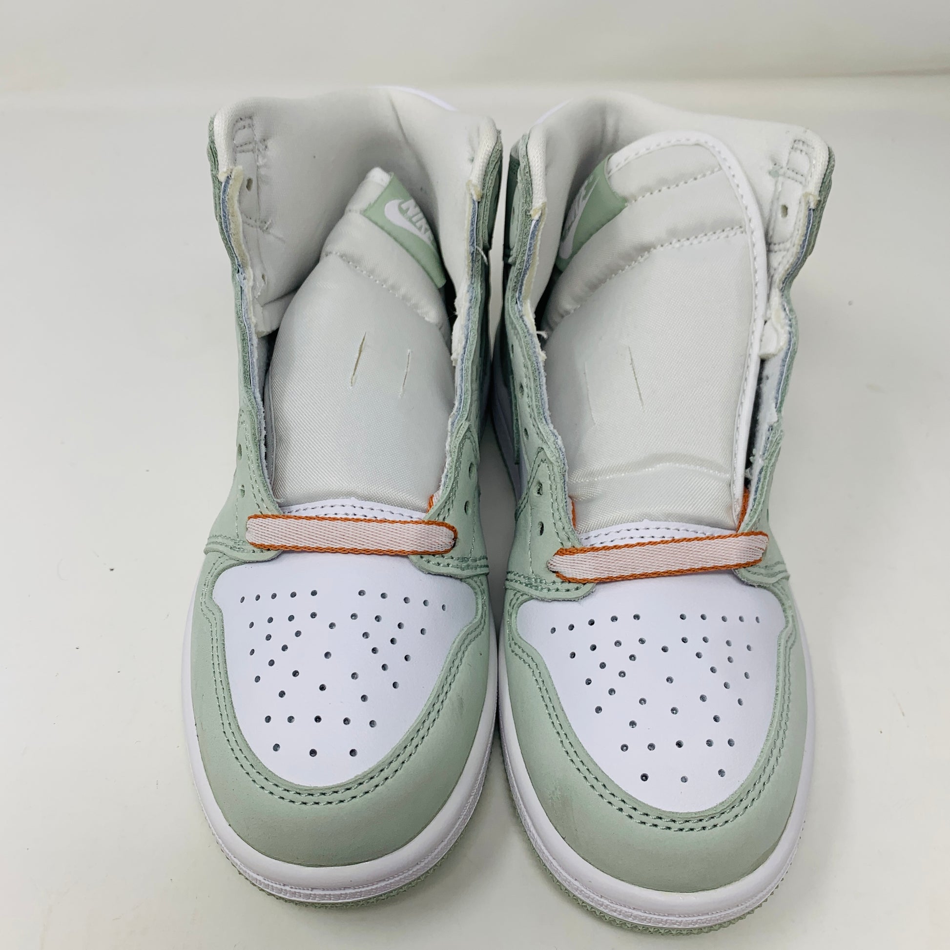 The Jordan 1 Retro High OG Seafoam (PS) sneakers by Jordan, in mint green and white with orange lace accents, are displayed side by side against a plain white background, with the tongues slightly raised.