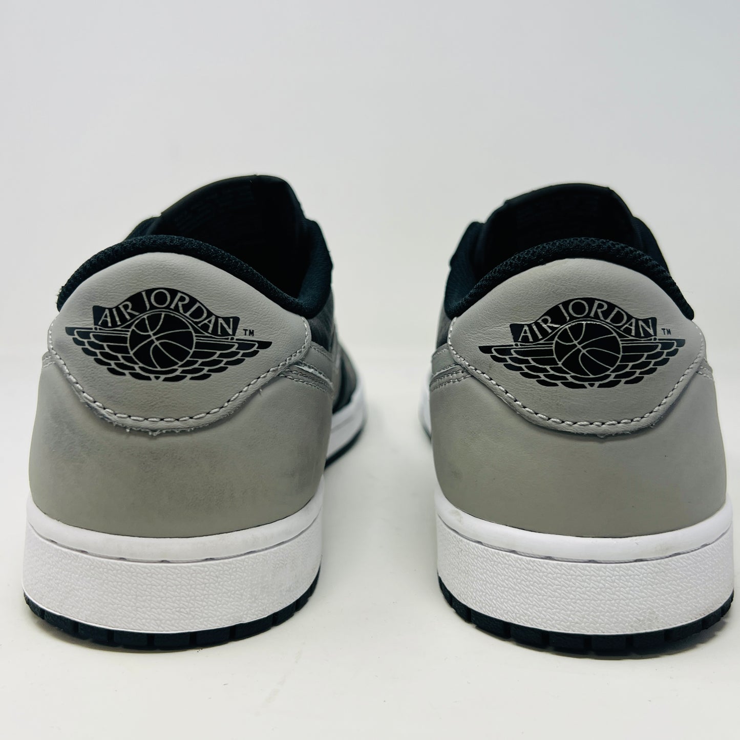 The Jordan 1 Retro Low OG Shadow (2024) sneakers in black and grey are displayed on a grey Nike box, showcasing clean uppers and matching laces. A small brown box complements the scene, with the visible size label enhancing authenticity.