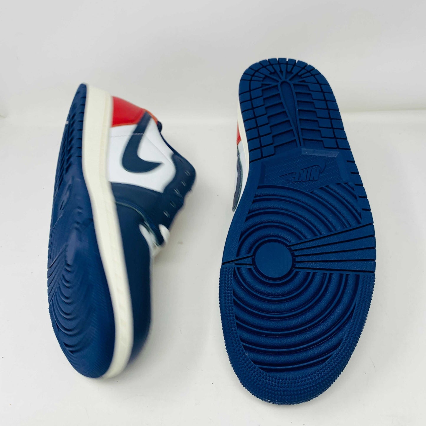 The Jordan 1 Retro Low OG Howard University sneaker, in navy, white, and red with a white midsole and Nike swoosh, rests on the shoe box. A small brown box with extra laces is placed in front.