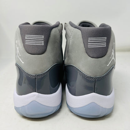 A pair of Jordan 11 Retro Cool Grey (2021) sneakers with white laces and translucent soles rest on a gray Nike Air box, showcasing the shiny patent leather and Jumpman logo. Size 9.5 appears on the label.