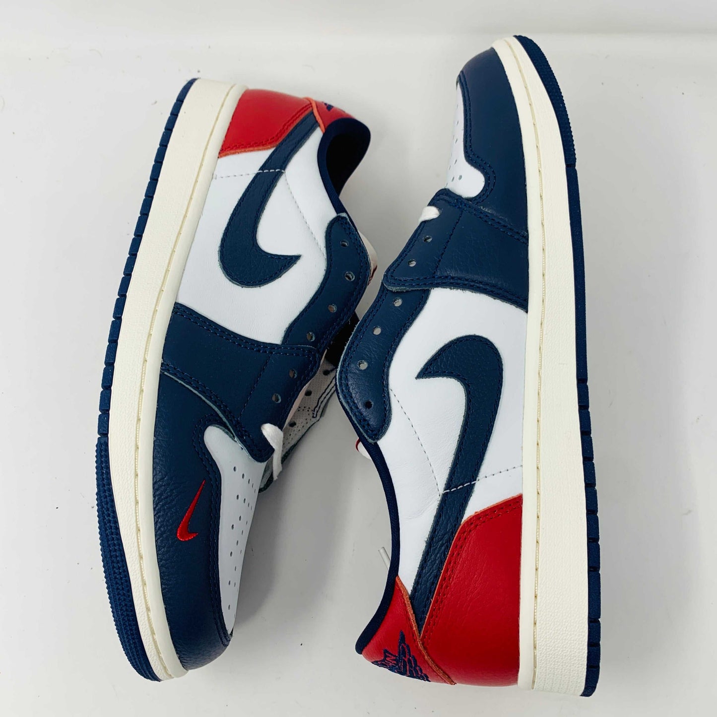 The Jordan 1 Retro Low OG Howard University sneaker, in navy, white, and red with a white midsole and Nike swoosh, rests on the shoe box. A small brown box with extra laces is placed in front.