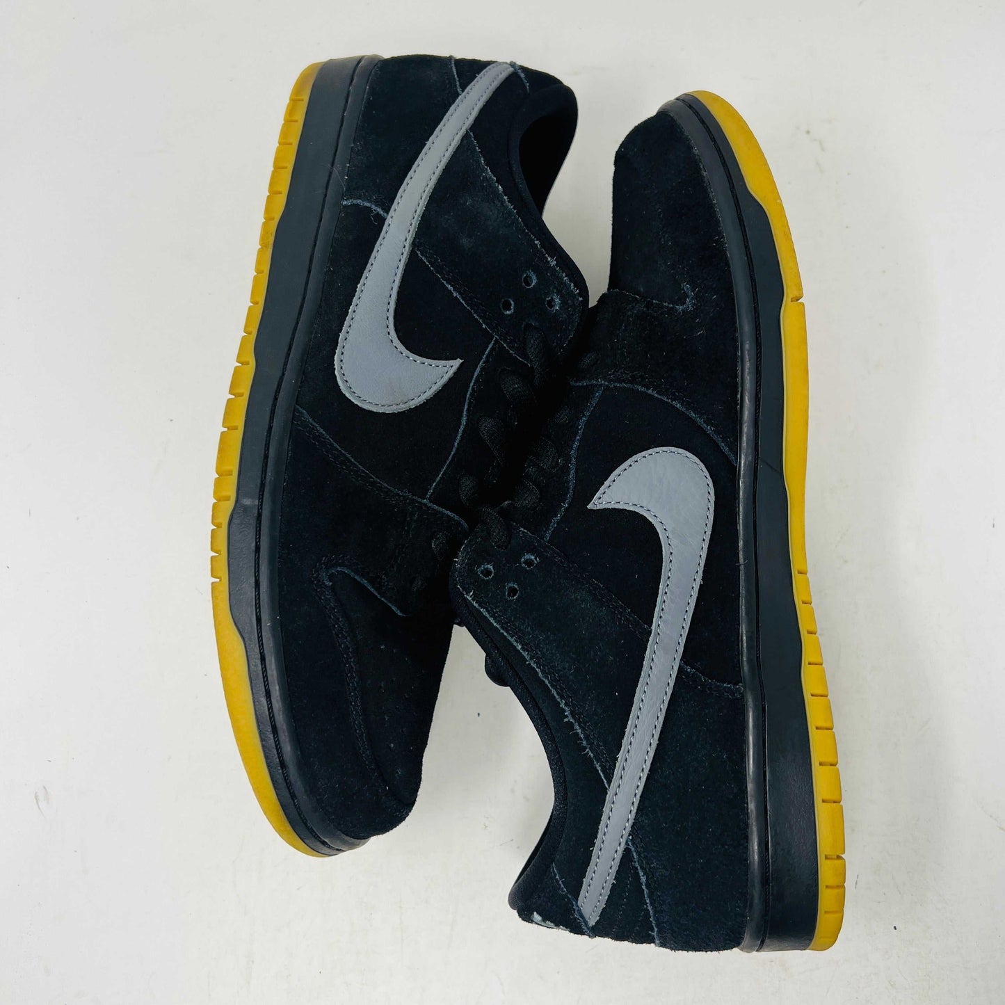 A pair of authentic Nike SB Dunk Low Fog sneakers in black with gray swoosh logos and vibrant yellow soles, accompanied by extra laces, displayed on a pristine white background from Holy Ground Sneaker Shop.