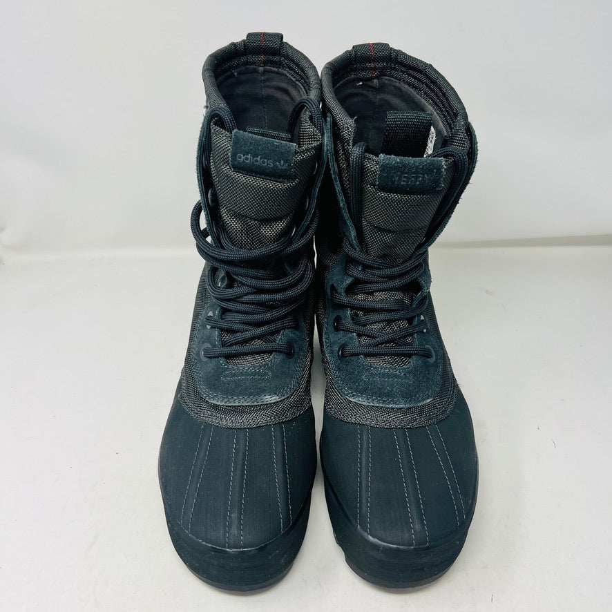 A 2015 Adidas Yeezy 950 Pirate Black boot is displayed on its box against a plain white background. This authentic Yeezy features a high lace-up design and sturdy ridged soles. The box includes size details, a partially visible label, and extra laces for added versatility.