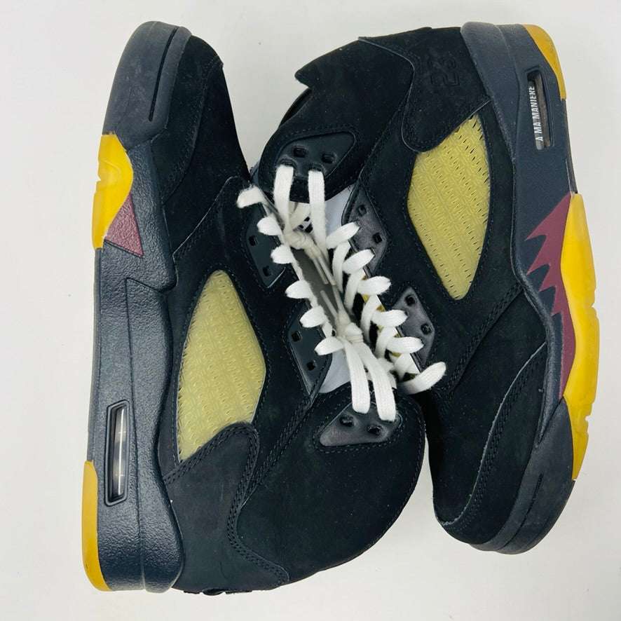 The Jordan 5 Retro A Ma Maniére Dusk high-tops feature black with yellow mesh panels, white laces, and colorful soles with purple and yellow details. Perfect for fashion enthusiasts, these stylish sneakers stand out against a white backdrop.