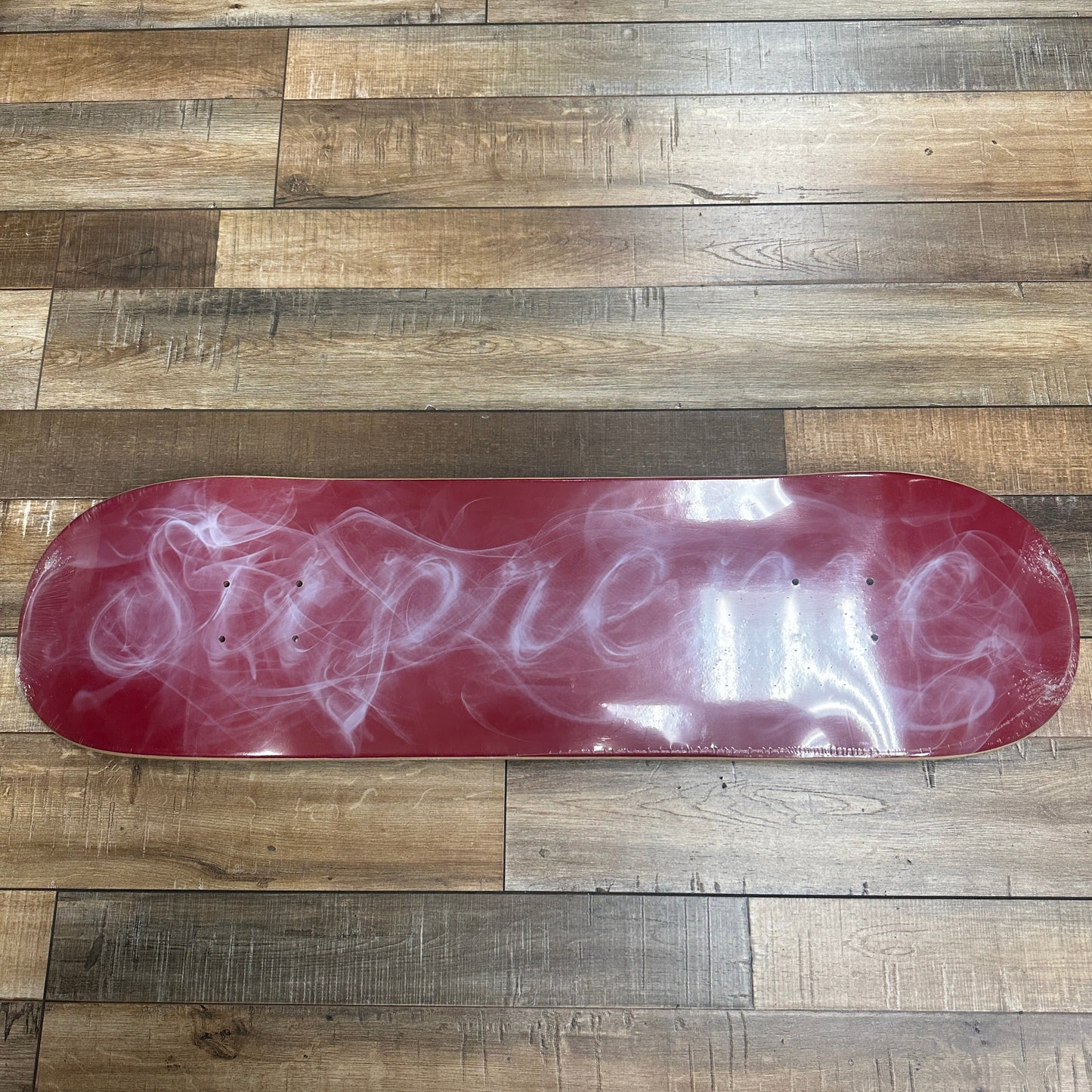 Supreme Smoke Skateboard Deck Red with smoke design on wood floor.