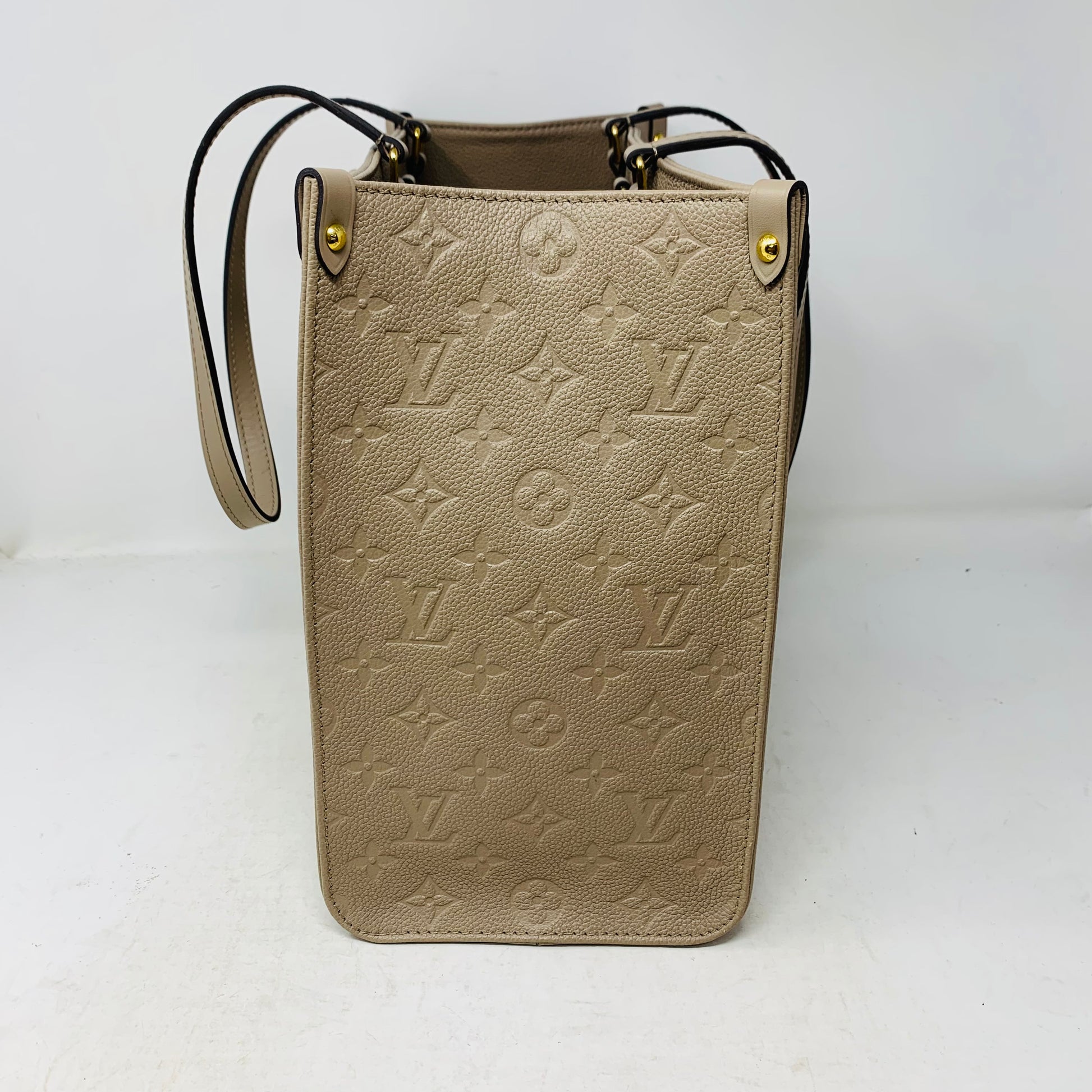 Explore the Louis Vuitton Onthego Tote PM in Tourterelle Beige Cream Leather with embossed Monogram Empreinte patterns. This elegant tote features a long strap, gold hardware, and a sophisticated white background.