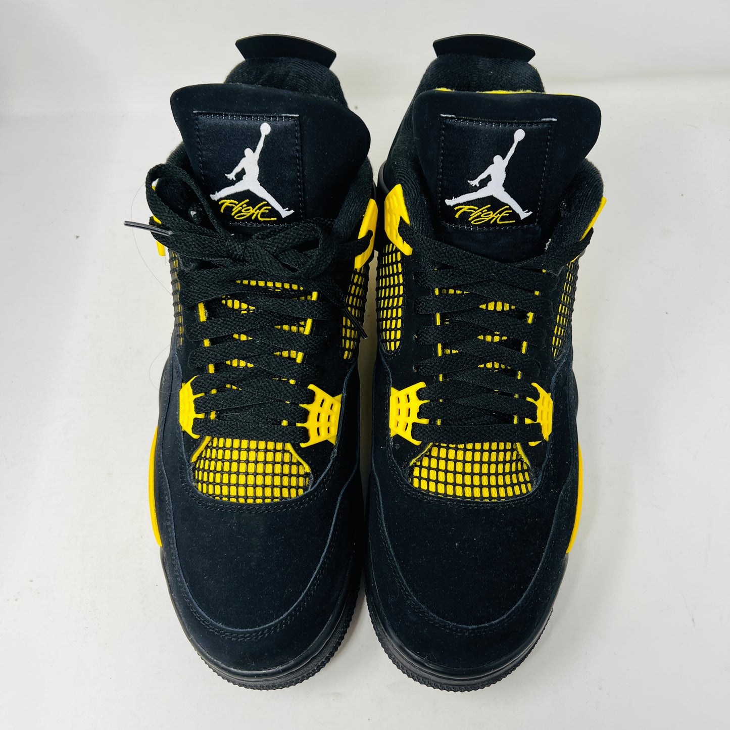 The Jordan 4 Retro Thunder (2023) features black uppers with yellow accents, a white sole, and visible air cushioning. It rests on a black and gray speckled shoebox in good condition and includes the distinctive wing design.