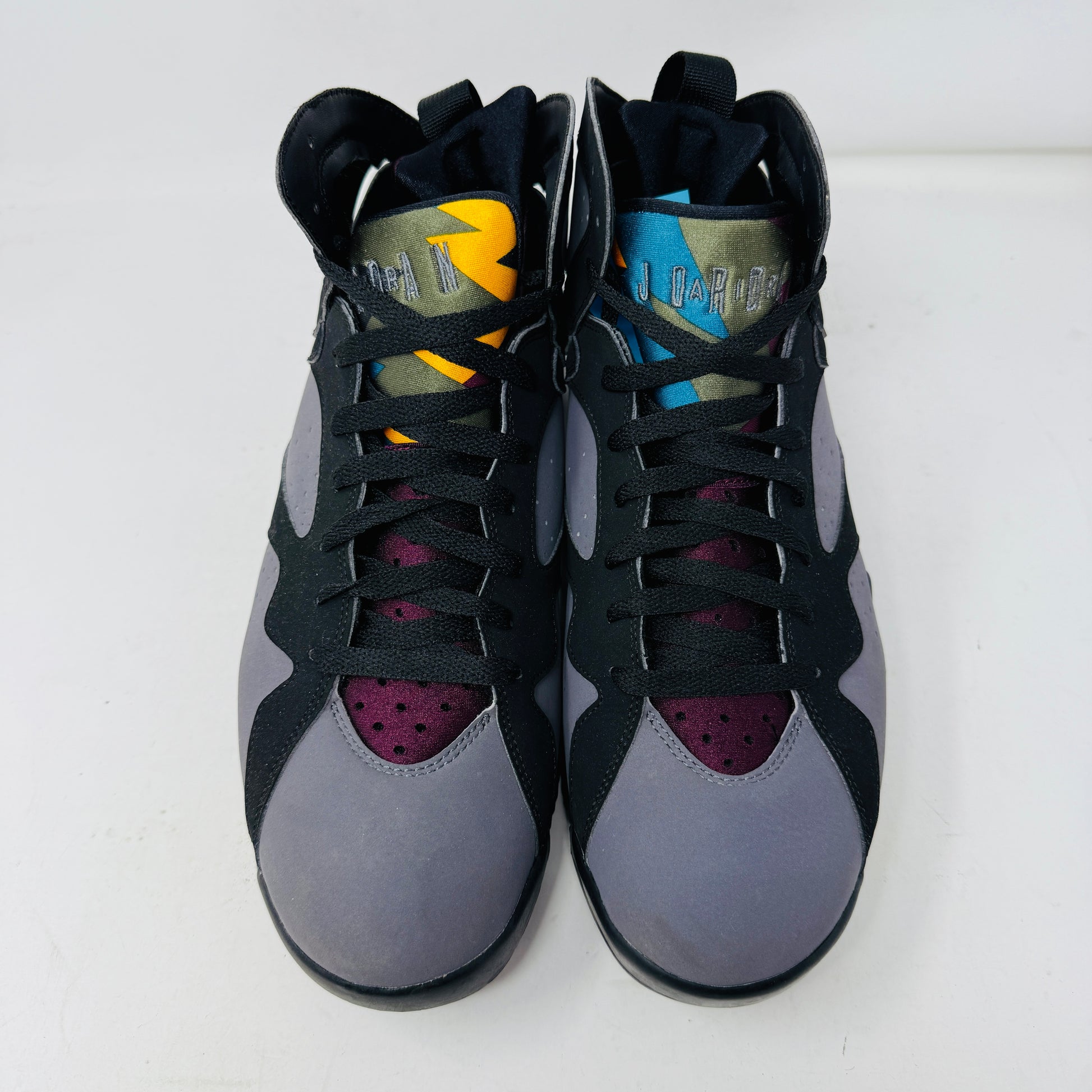 The Jordan 7 Retro Bordeaux (2015) sneakers, in black and gray with maroon accents and the Jumpman logo, feature angular midsoles, dark laces, and sleek uppers. They evoke a 2015 vibe and are photographed side by side on a white background.