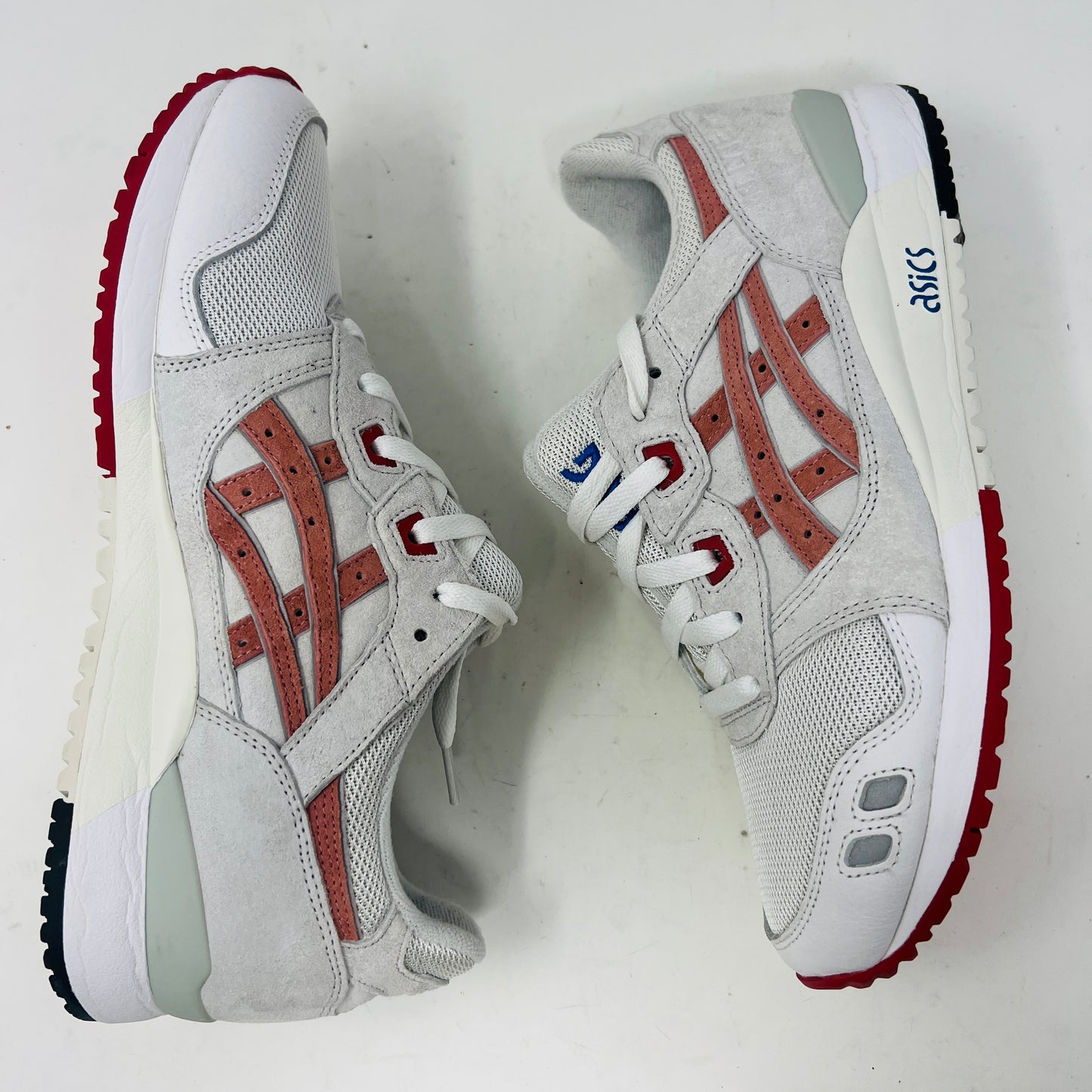 The ASICS Gel-Lyte III Ronnie Fieg Tokyo Trio Yoshino Rose sneaker, featuring clean white and beige uppers with red accents and pink iconic stripes, sits on its box. It includes navy, pink, and beige extra laces, with the authentic size clearly displayed on the box.