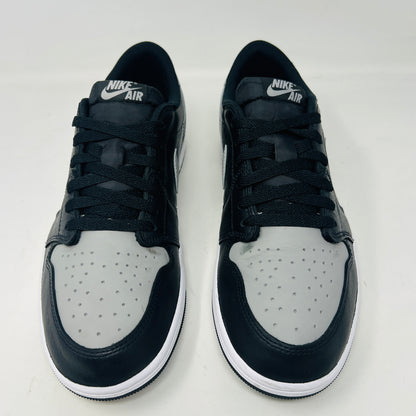 The Jordan 1 Retro Low OG Shadow (2024) sneakers in black and grey are displayed on a grey Nike box, showcasing clean uppers and matching laces. A small brown box complements the scene, with the visible size label enhancing authenticity.