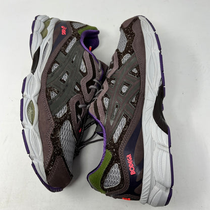 The ASICS Gel-NYC Bodega After-Hours sneakers, in brown with gray, purple, and green accents, sit on a box. A packet of extra red laces is attached. The size and details are prominently shown on the label.