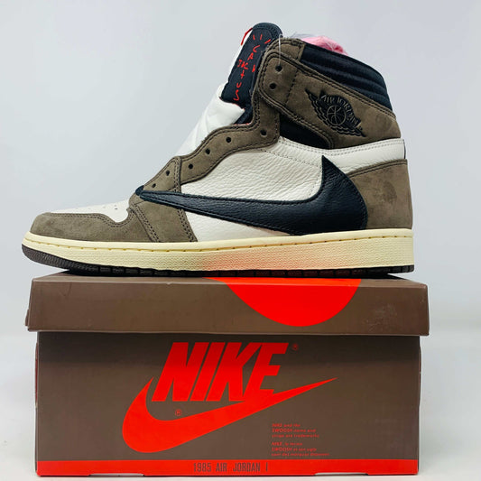 A pair of authentic Jordan 1 High Travis Scott Mocha sneakers in brown, white, and black is displayed on an orange and brown Nike shoebox. These feature a distinctive reversed black Swoosh and come with extra laces for versatile styling.