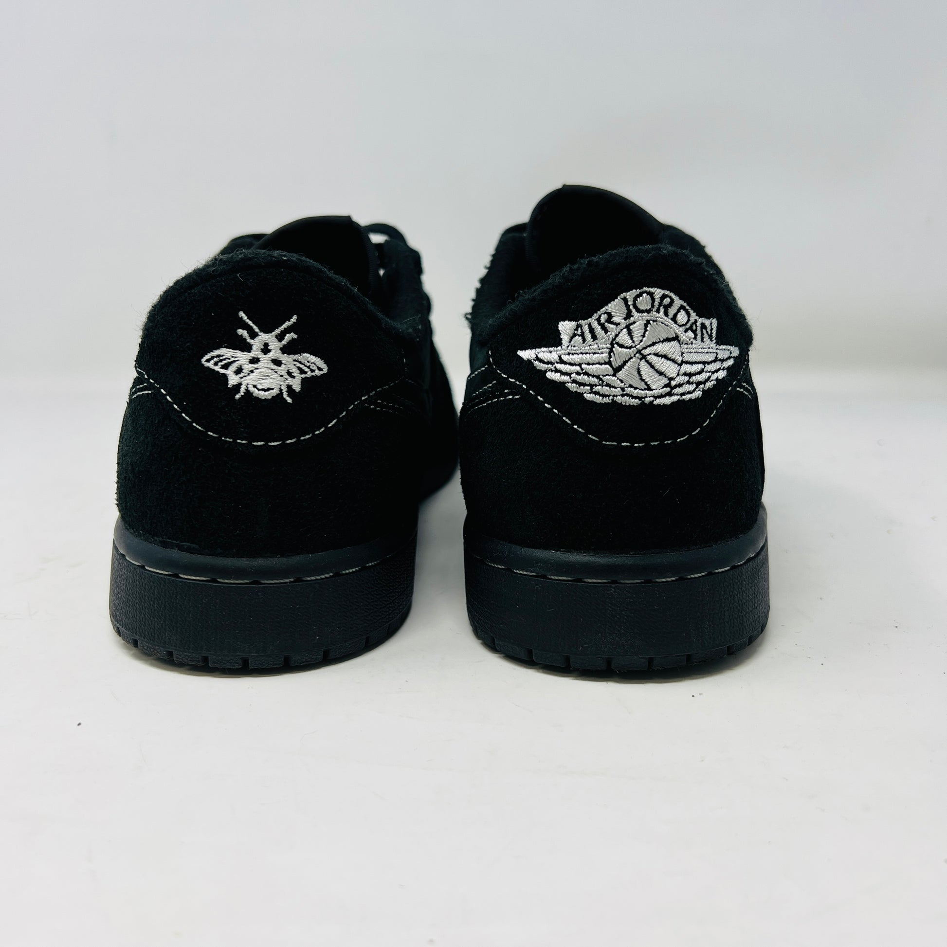 The Jordan 1 Retro Low OG SP Travis Scott Black Phantom sneaker, featuring clean black uppers with white stitching, is displayed on a black shoe box. It includes two sets of laces—one red and the other in a black-and-white pattern.