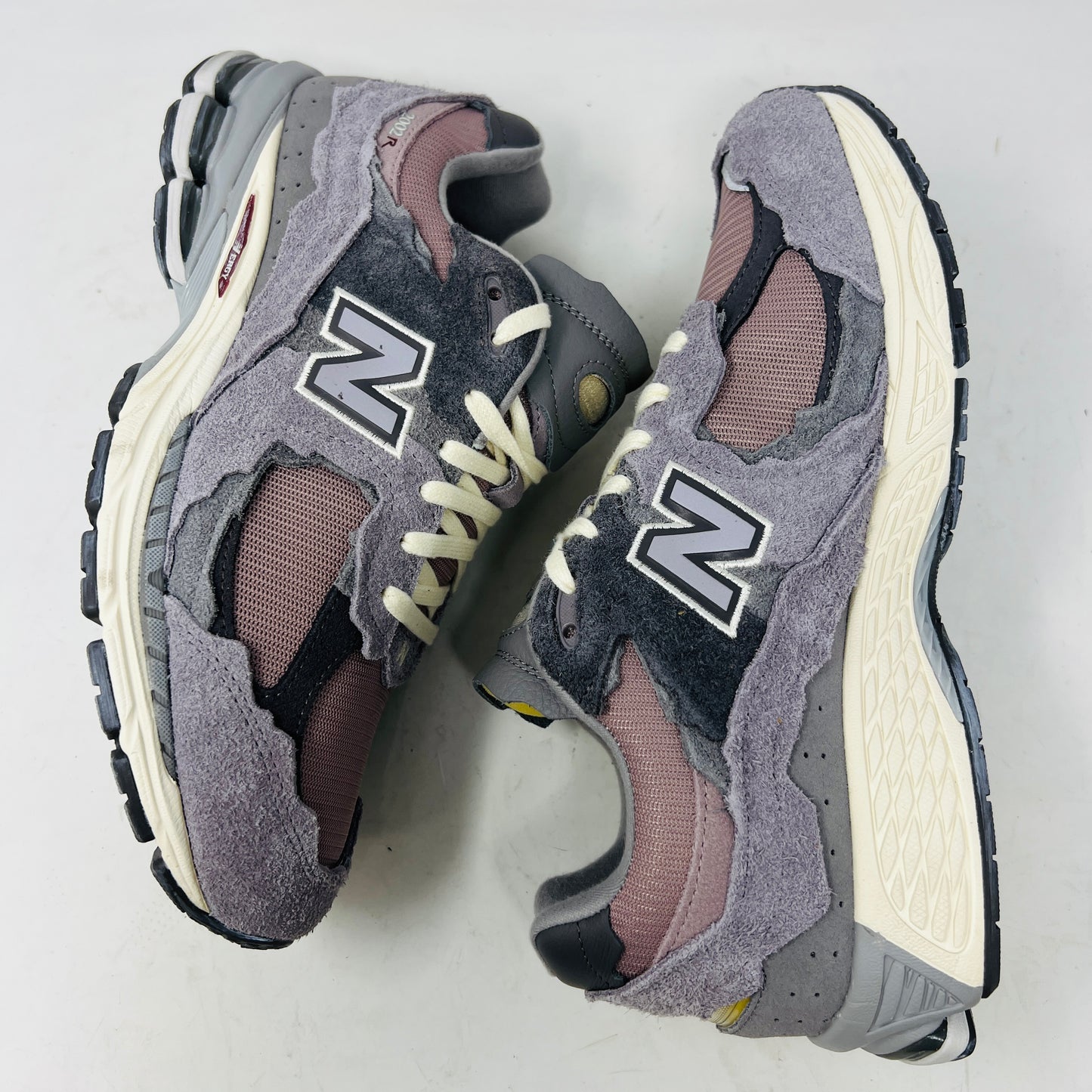 A pair of New Balance 2002R Protection Pack Lunar New Year Dusty Lilac sneakers mix gray and beige tones with CLEAN UPPERS and a textured design. Displayed on a shoebox, they include extra maroon laces. The box label details the shoe size and model.