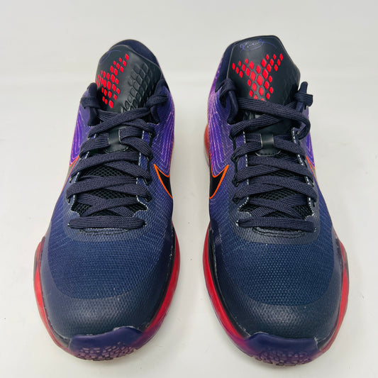 The Nike Kobe 10 Hero (GS) sneaker from 2015 in purple and pink with orange accents rests on a black shoebox. It features clean uppers, a prominent black Nike swoosh, and sits atop a translucent red sole. The size label reads 7Y, indicating light wear.