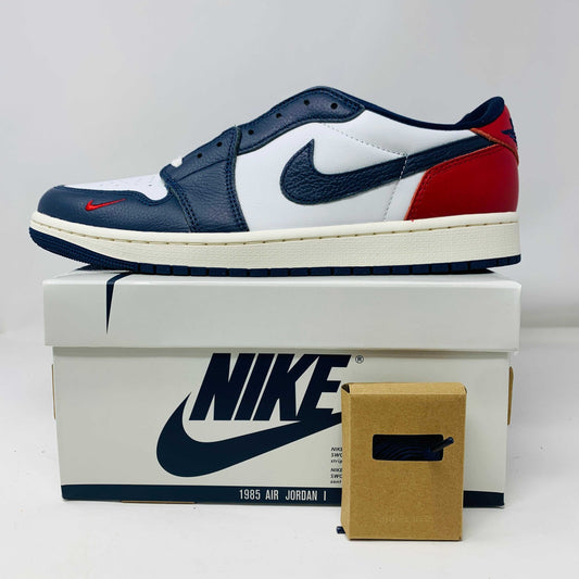 The Jordan 1 Retro Low OG Howard University sneaker, in navy, white, and red with a white midsole and Nike swoosh, rests on the shoe box. A small brown box with extra laces is placed in front.