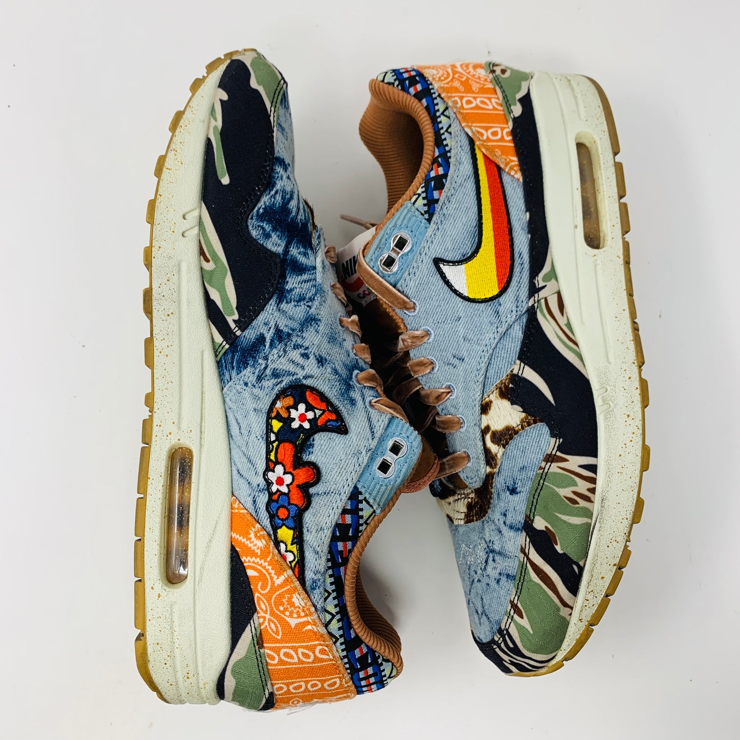 The Nike Air Max 1 SP Concepts Heavy sneakers boast a colorful patchwork design with denim, camouflage, and animal prints in vibrant orange, blue, and yellow hues. They feature distinctive swoosh logos on the sides.