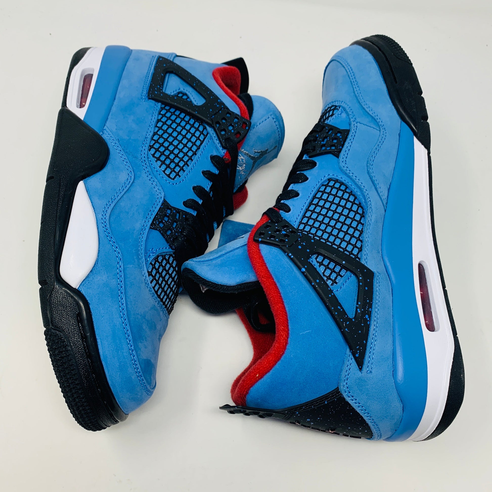 The Jordan 4 Retro Travis Scott Cactus Jack sneaker in blue, accented with black and red, features a visible air unit in the heel and a Jumpman logo hang tag, packaged in a black speckled box with an orange Jumpman logo and AIR.