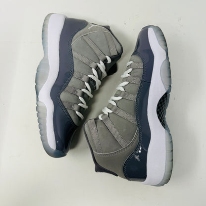 The Jordan 11 Retro Cool Grey (2021) (GS) sneakers by Jordan feature glossy patent leather overlays, a Jumpman logo on the heel, clean white uppers, and laces. They are displayed on a pristine Nike shoebox with size and model details labeled.