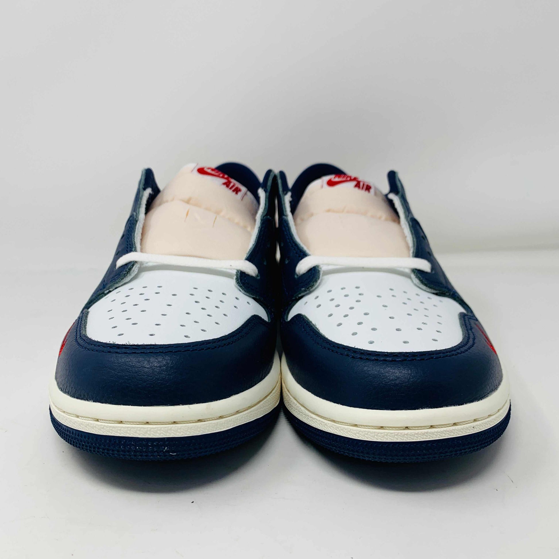 The Jordan 1 Retro Low OG Howard University sneaker, in navy, white, and red with a white midsole and Nike swoosh, rests on the shoe box. A small brown box with extra laces is placed in front.