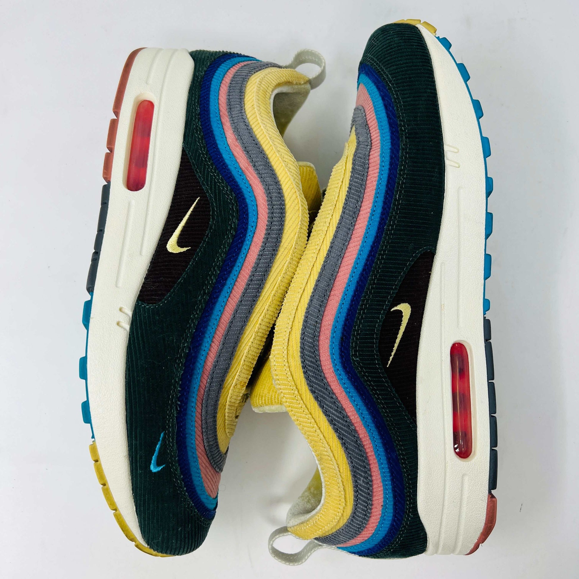 The Nike Air Max 1/97 Sean Wotherspoon sneakers, from Nike, feature a blend of blue, pink, yellow, and black patterns with a textured design. They include a visible air unit in the midsole, a prominent swoosh logo on the side, extra laces, and blue-detailed soles.