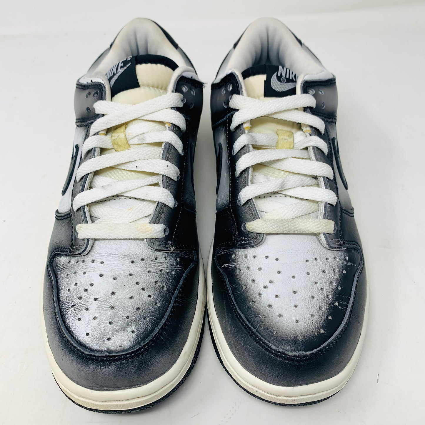 The Nike Dunk Low Haze 2003 sneakers, displayed side by side, feature a black and white design with white laces. They have perforated toe boxes and visible logos on the tongue against a plain white background.