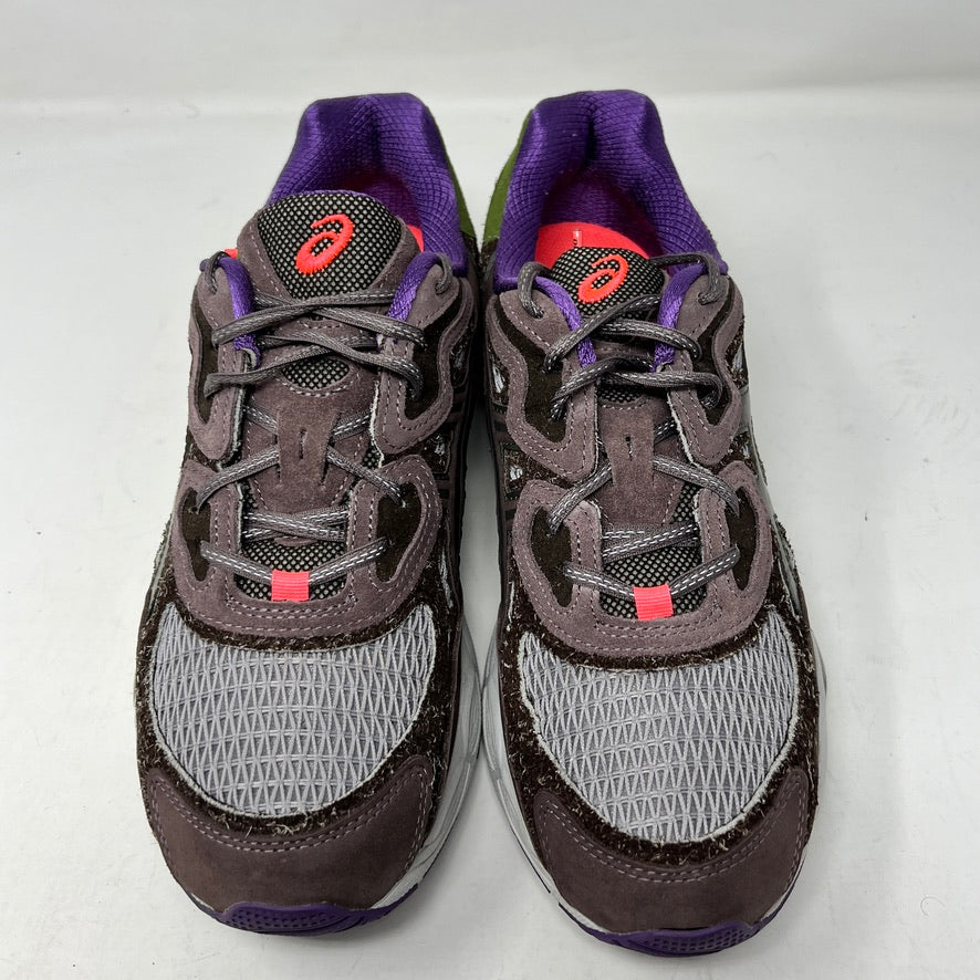 The ASICS Gel-NYC Bodega After-Hours sneakers, in brown with gray, purple, and green accents, sit on a box. A packet of extra red laces is attached. The size and details are prominently shown on the label.